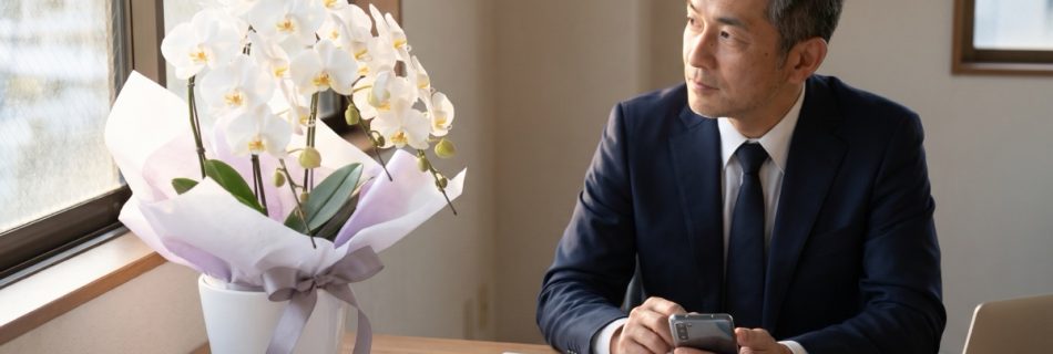 白い胡蝶蘭のお供え花を前に、供花の手配を考えるスーツ姿の中年男性